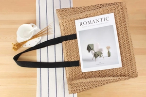 Detail of woven straw tote bag with black canvas handles on a wooden table setup