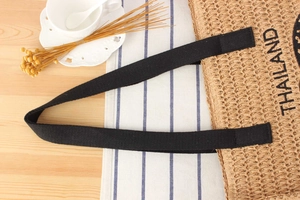 Detail of woven straw bag with black canvas straps and printed Thailand lettering