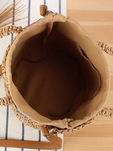 Handwoven straw tote bag with brown leather strap and canvas lining on wooden background