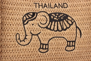 Detail of woven straw bag showing black Thailand elephant embroidery and natural texture
