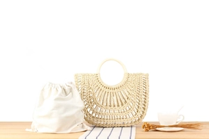 Detail of half-moon woven straw bag with circular handles and cotton drawstring liner