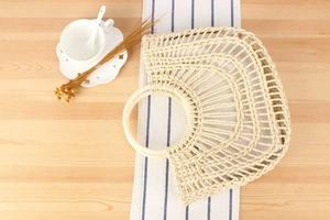 Detailed close-up of a semi-circular woven straw handbag with a round handle on a table