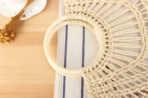 Close-up of beige woven handbag texture with smooth round handles and bohemian design