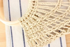 Detailed close-up of cream woven mesh handbag featuring a smooth yellow round handle