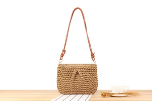Detail view of woven straw shoulder bag with leather strap and knot on wooden table