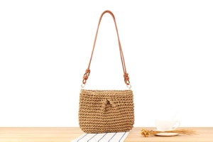 Detailed view of woven shoulder bag with leather straps on a minimalist wooden table