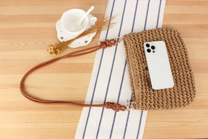 Detail view of woven straw crossbody bag with leather strap and zipper closure on wooden table