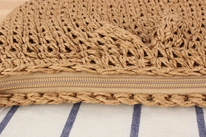 Detailed close-up of woven straw handbag texture and secure metal zipper closure