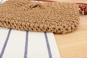 Detailed close-up of tan woven straw bag texture with brown leather strap and metal buckle