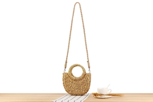 Détail du sac en paille demi-lune avec poignées rondes sur une table en bois