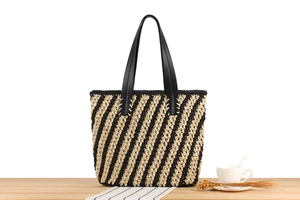 Detailed view of the woven straw tote bag with black and beige diagonal stripes on wood