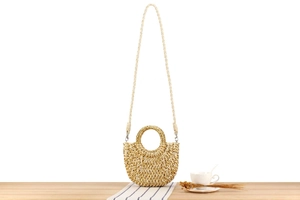 Détail du sac en paille demi-lune avec fil doré sur fond de table en bois rustique