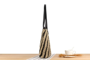 Detail of a large striped woven tote bag with black leather straps on a wooden surface