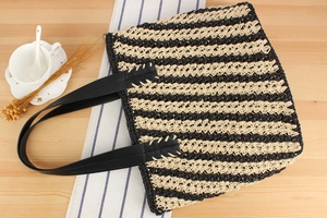 Detailed view of striped woven tote bag with premium black leather handles and texture