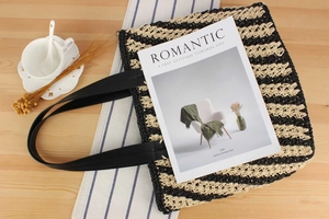 Close-up of contrast striped straw beach bag with black handles on a wooden table