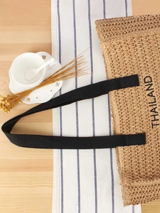 Handwoven straw tote bag with black straps and Thailand lettering on a cafe table