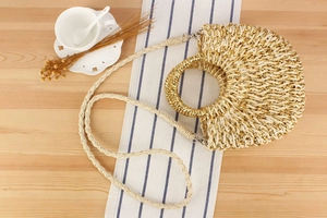 Détail macro du sac en paille tressée main avec fibres dorées et bandoulière beige