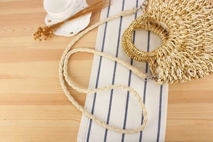 Détail du sac en paille avec fils dorés, poignées rondes et bandoulière sur la table