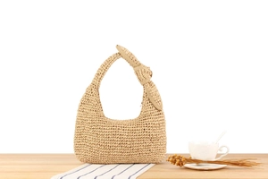 Detailed close-up of woven hobo handbag with large decorative bow on wooden table