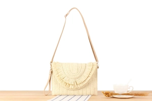 Detail view of woven straw envelope bag with decorative fringe and adjustable strap