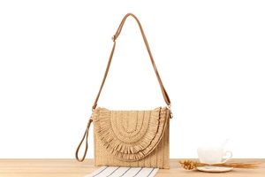 Detail of straw woven crossbody bag with brown leather strap and layered tassel trim