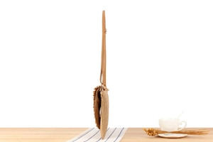 Detail view of a slim khaki woven straw crossbody bag in a summer vacation lifestyle setting