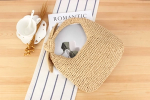Detail of hand-woven straw hobo bag with knot handle on a rustic wooden table setup