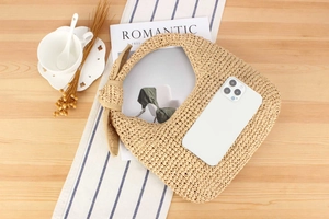 Detailed view of beige hand-woven straw bag with large knot on a wood surface
