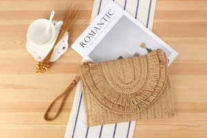 Detailed view of handmade woven straw clutch with layered tassels on a light wooden table