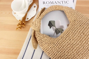 Detail of beige woven hobo bag with knotted strap on wooden desk with romantic summer props