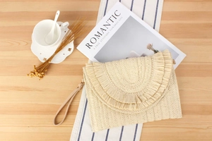 Detail of cream straw envelope bag with bohemian fringe on a rustic wooden table