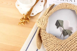 Detail of hand-woven beige straw handbag with knotted handle and crescent moon shape