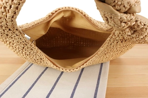 Close-up of woven straw handbag with knotted handle detail and zipper closure