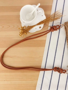 Brown hand-woven shoulder bag with slim leather strap on a minimalist wooden table setting