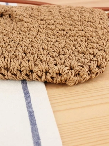 Minimalist woven straw bag with leather straps on a rustic wooden table setting