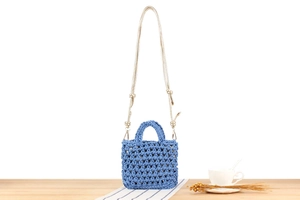 Blue crochet mini handbag with gold chain strap shown on a wooden table setup