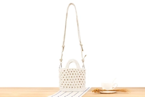Detail of white handmade crochet mini bag with golden chain on a natural wooden surface