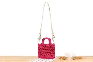 Close-up of handmade pink woven mini bag with crochet texture and gold shoulder strap