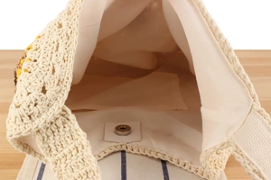 Close-up of cream woven bag interior with magnetic clasp and floral crochet detail