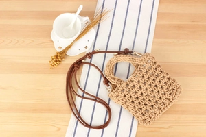 Detail of hand-woven cotton rope bag featuring a brown leather strap and metallic buckle