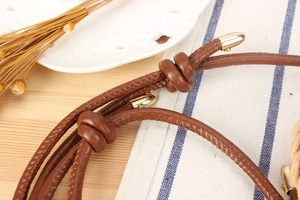 Detail of woven brown leather strap with golden metal caps and intricate stitching