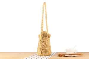 Close-up of beige handmade straw bucket bag with floral weave details on a wooden table