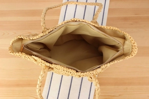 Detail view of woven straw tote bag featuring beige fabric lining and metal zipper closure