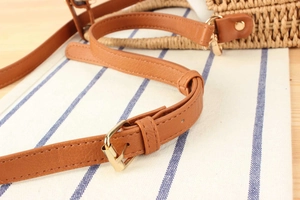 Dettaglio della tracolla in pelle marrone con fibbia dorata su borsa in paglia intrecciata