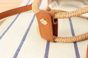 Dettaglio borsa in paglia intrecciata con cinturino in pelle marrone e fibbia oro