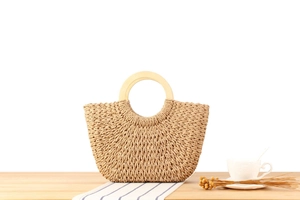 Detailansicht der Strohtasche mit runden Holzgriffen auf einem dezenten Holztisch