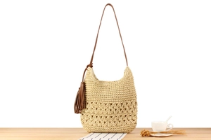 Detail of a beige woven shoulder bag with hollow patterns and a brown leather tassel