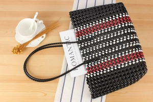 Flat lay of a black hand-woven tote bag with red and white lattice accents on wood
