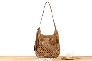 Detail of hand-woven straw shoulder bag with leather tassel and brown strap on wood table