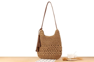 Detail of hand-woven straw shoulder bag featuring diamond cut-outs and a large tassel